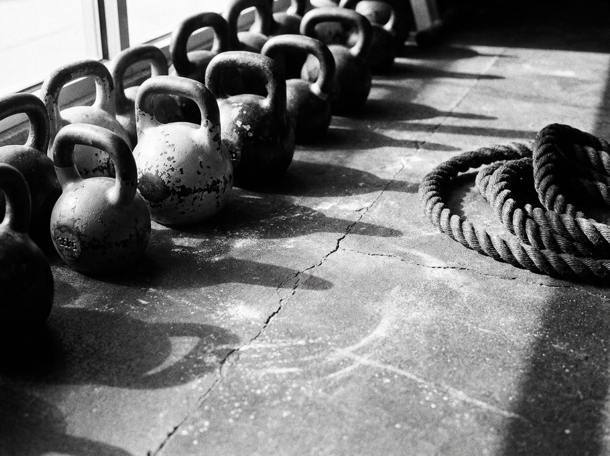 Rows of worn kettlebells and a battle rope on a chalk-marked concrete floor
