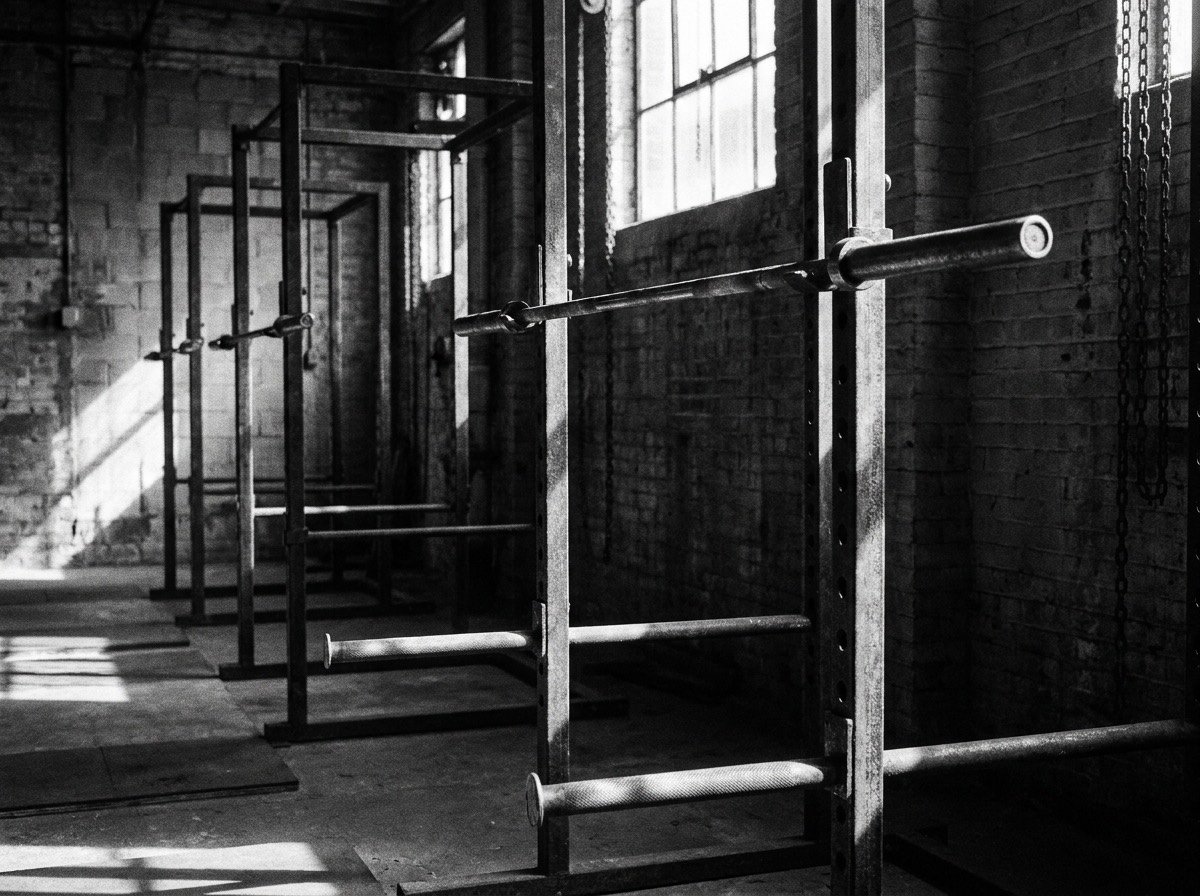 A row of steel squat racks with loaded barbells in window light